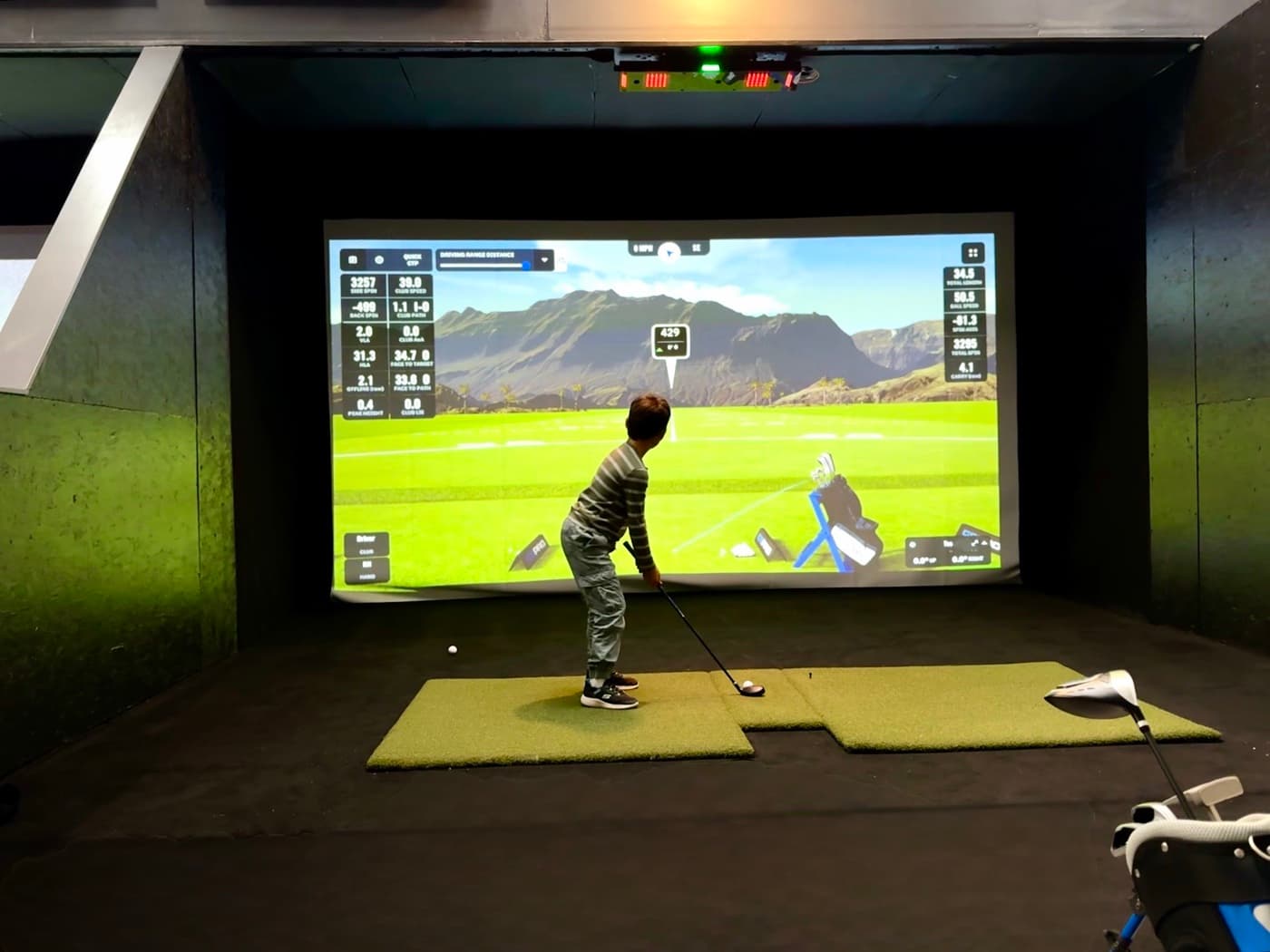 A junior golfer hitting a shot in an indoor simulator bay